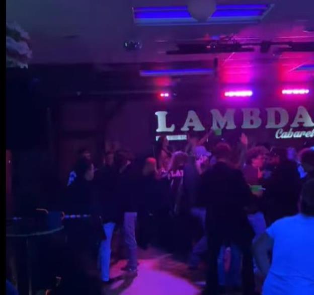 A video still shows a number of people dancing in a dark club in front of a sign that reads 