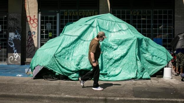 A man walks past a green tent on the street.